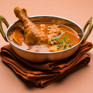Spicy Reddish Chicken Curry or Masala, with prominent Leg Piece, served in a bowl or Kadhai over colourful or wooden background. selective focus.
